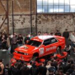 BMW E30 M3 com pintura Jägermeister é exibido apoiado em quatro motos Suzuki GSX-R na Ultrace Germany