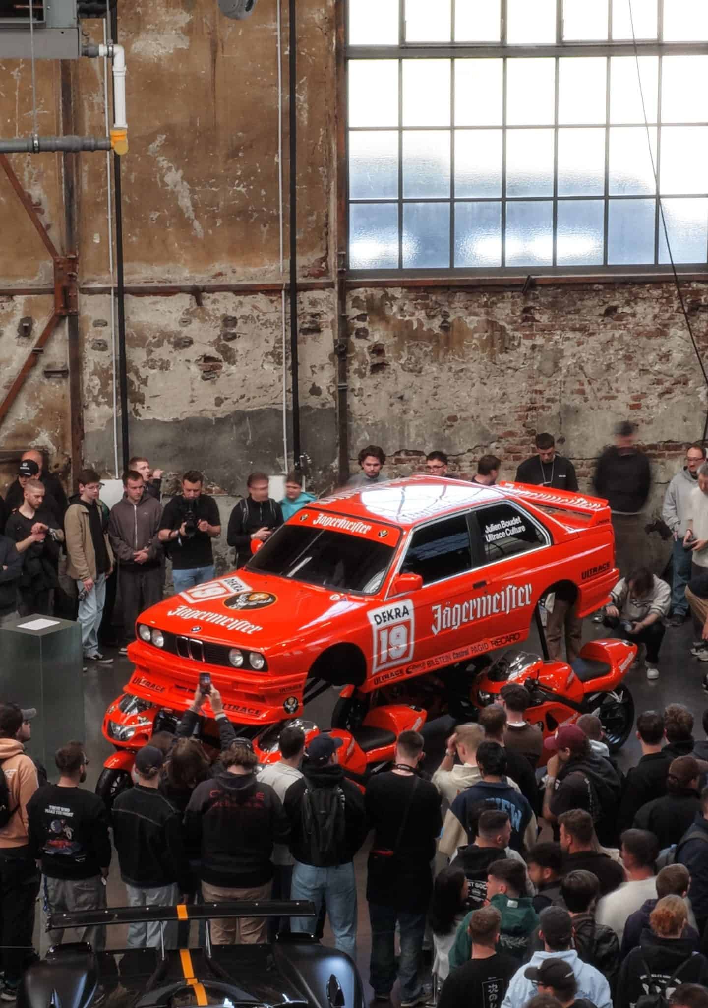 BMW E30 M3 com pintura Jägermeister é exibido apoiado em quatro motos Suzuki GSX-R na Ultrace Germany - Imagem do artigo original